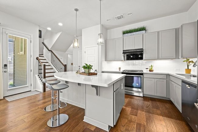 Kitchen featuring appliances with stainless steel finishes, gray cabinetry, dark wood finished floors, a kitchen island, and tasteful backsplash | Image 11