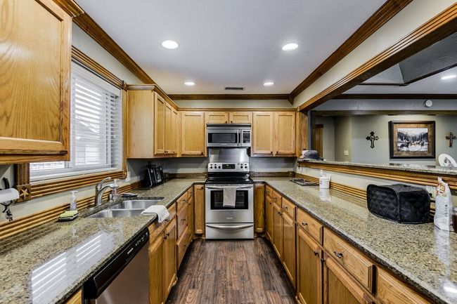 Kitchen with stainless steel appliances, crown molding, dark wood finished floors, light stone countertops, and recessed lighting | Image 11
