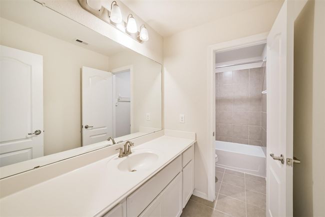 The upstairs secondary bathroom features a modern design with a large mirror above a sleek vanity, ample counter space, and a well-lit atmosphere. It includes a bathtub with tiled walls, creating a clean and inviting space. | Image 22
