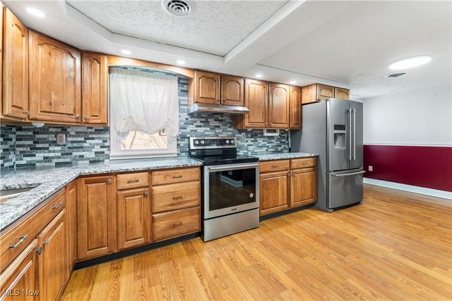 Kitchen featuring under cabinet range hood, brown cabinetry, baseboards, a textured ceiling, and appliances with stainless steel finishes | Image 18