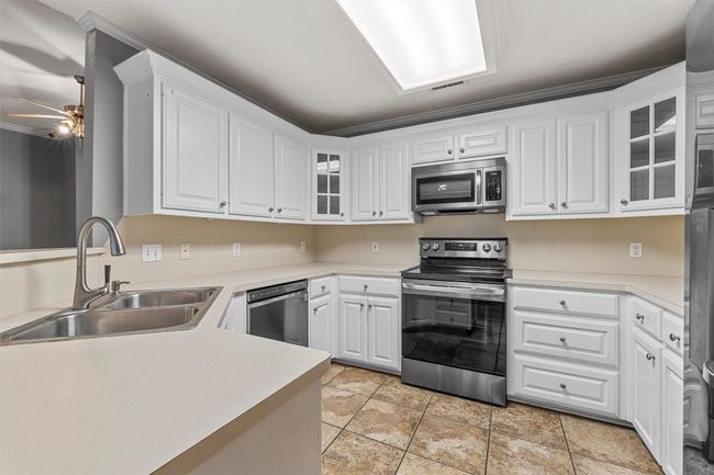 Kitchen featuring stainless steel appliances, ceiling fan, white cabinetry, crown molding, and light tile patterned flooring | Image 7