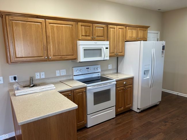 kitchen with brown cabinets, light countertops, white appliances, and dark wood-type flooring | Image 5