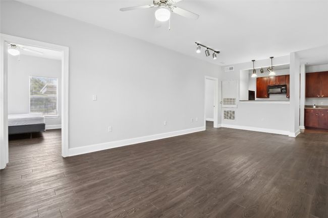 Unfurnished living room with dark wood-style floors, baseboards, and ceiling fan | Image 11