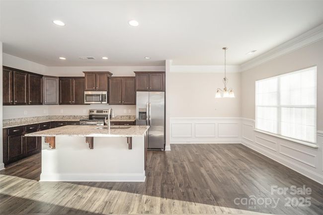 Wide angle view from the family room of the kitchen and adjouring breakfast area adorned with window box and chair rail decorum. | Image 10