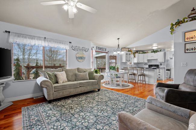 Living area featuring light wood finished floors, ceiling fan with notable chandelier, lofted ceiling, and baseboards | Image 6