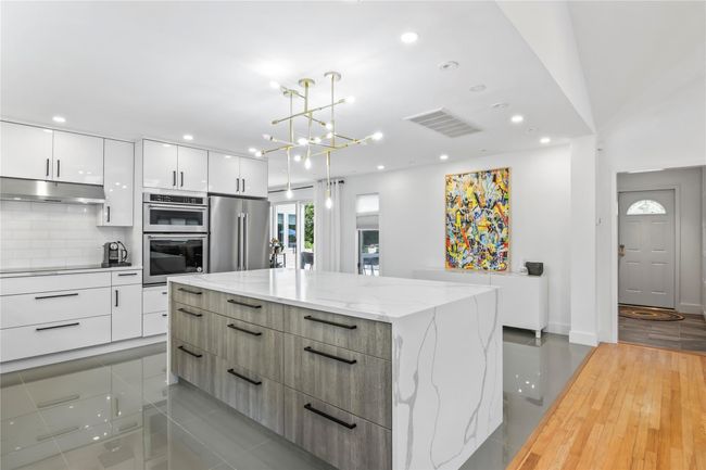 Kitchen with modern cabinets, stainless steel appliances, under cabinet range hood, white cabinets, and a center island | Image 9