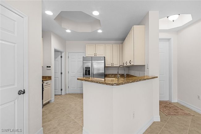 Kitchen featuring stainless steel fridge, dark stone countertops, light tile patterned floors, a peninsula, and recessed lighting | Image 6