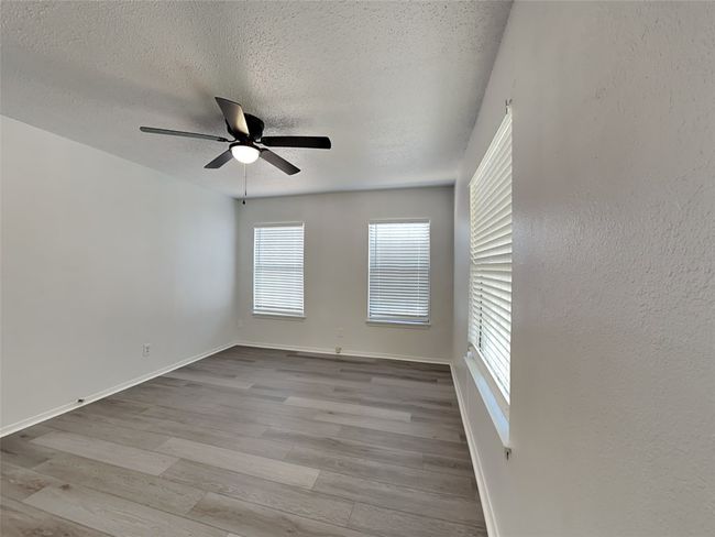 Empty room with wood finished floors, ceiling fan, a textured ceiling, and baseboards | Image 12