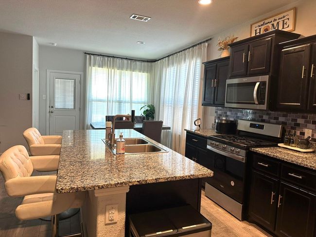 Kitchen with appliances with stainless steel finishes, a breakfast bar, decorative backsplash, a center island with sink, and light stone counters | Image 14