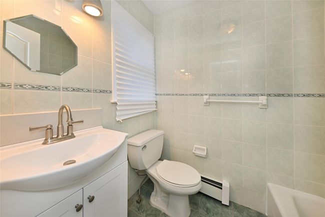 Full bath featuring a baseboard heating unit, tile walls, toilet, a bath, and vanity | Image 22