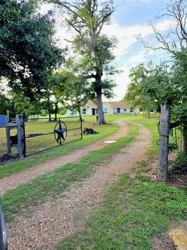 Charming rural property with a gravel driveway leading to a cozy house surrounded by lush greenery. A gated entrance with a star emblem adds rustic appeal. Ideal for those seeking tranquility and natural beauty. Whit electric gate. | Image 29