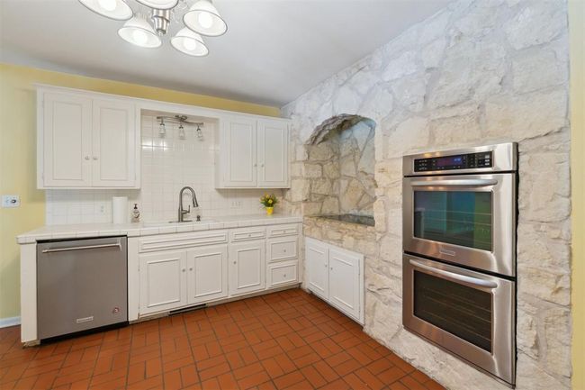 Kitchen featuring stainless steel appliances, tile countertops, white cabinetry, a chandelier, and backsplash | Image 12