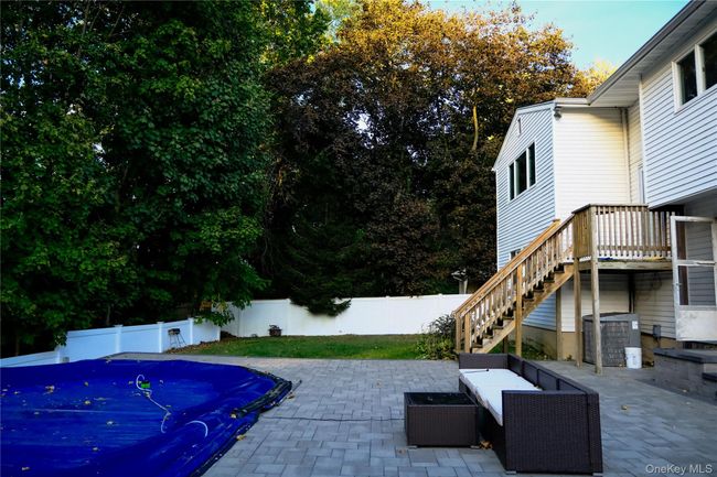 Fenced backyard featuring a patio area, a covered pool, stairs, view of scattered trees, and a deck | Image 5