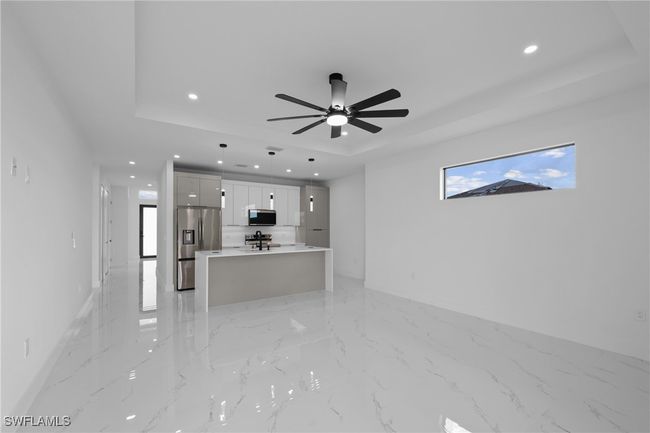 Unfurnished living room with a tray ceiling, recessed lighting, ceiling fan, baseboards, and light marble finish flooring | Image 14