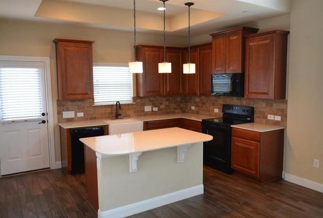Kitchen featuring black appliances, a sink, dark wood-style flooring, a tray ceiling, and light countertops | Image 5