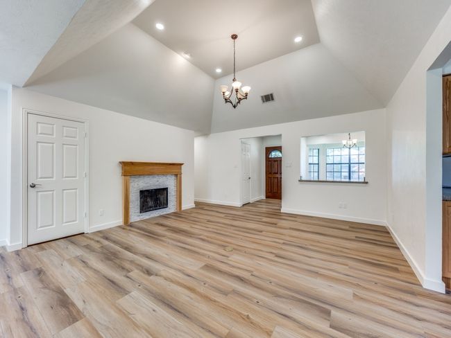 Unfurnished living room with a chandelier, a fireplace, light wood-style flooring, high vaulted ceiling, and recessed lighting | Image 7