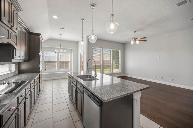 Kitchen featuring visible vents, black electric stovetop, dishwasher, ceiling fan with notable chandelier, and a sink | Image 18