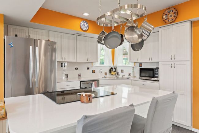 Kitchen featuring light countertops, a sink, tasteful backsplash, a breakfast bar, and appliances with stainless steel finishes | Image 10