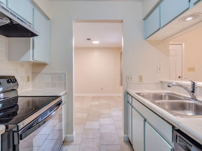 Kitchen with black electric range oven, under cabinet range hood, tile countertops, a sink, and blue cabinetry | Image 8