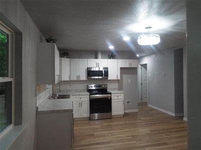 Kitchen with light hardwood / wood-style flooring, stainless steel appliances, white cabinets, and sink | Image 3