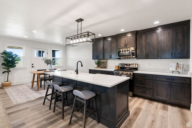 Kitchen featuring stainless steel appliances, light wood finished floors, a kitchen bar, light countertops, and recessed lighting | Image 7
