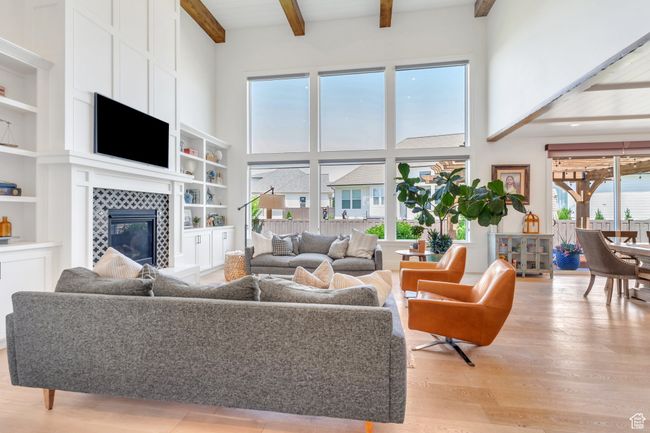Living room featuring a high ceiling, light wood-style floors, beam ceiling, a tile fireplace, and built in shelves | Image 9
