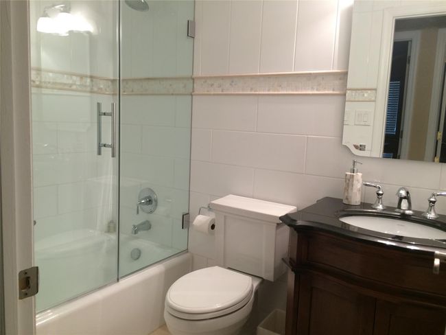 Bathroom with tile walls, vanity, shower / bath combination with glass door, tasteful backsplash, and toilet | Image 11