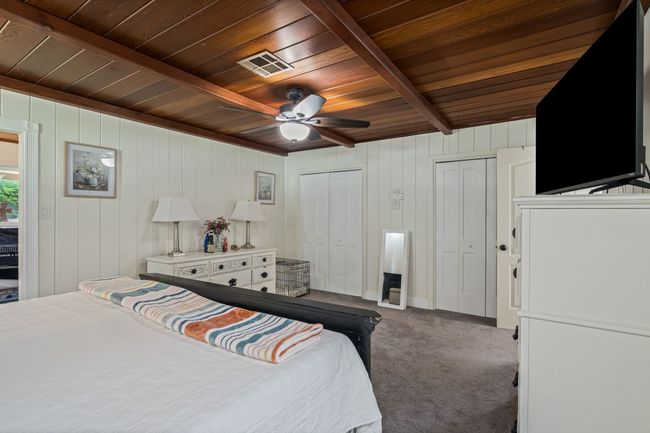 Bedroom with a wooden ceiling with exposed beams, two closets, dark colored carpet, wooden walls, and a ceiling fan | Image 17