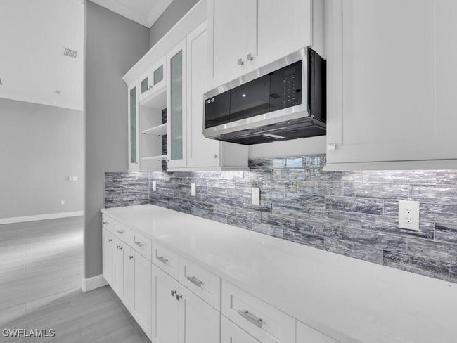 Kitchen featuring stainless steel microwave, backsplash, white cabinets, and glass insert cabinets | Image 13