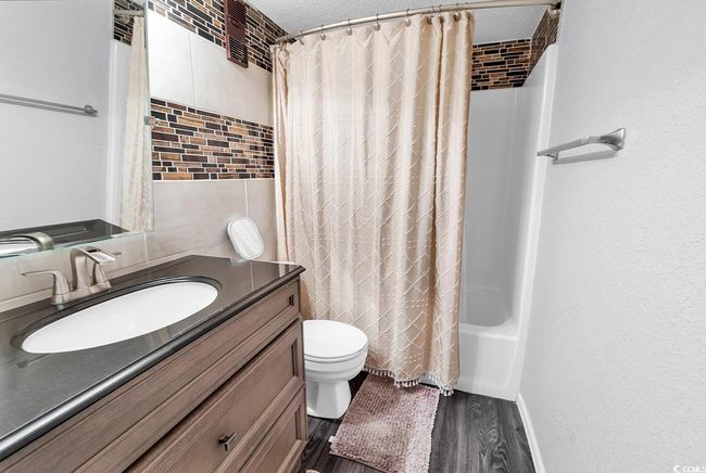 Bathroom featuring shower / bath combo, a textured ceiling, toilet, wood finished floors, and vanity | Image 7