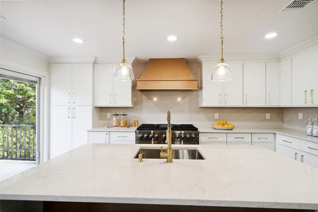 Kitchen featuring custom range hood, range, a center island with sink, tasteful backsplash, and decorative light fixtures | Image 17