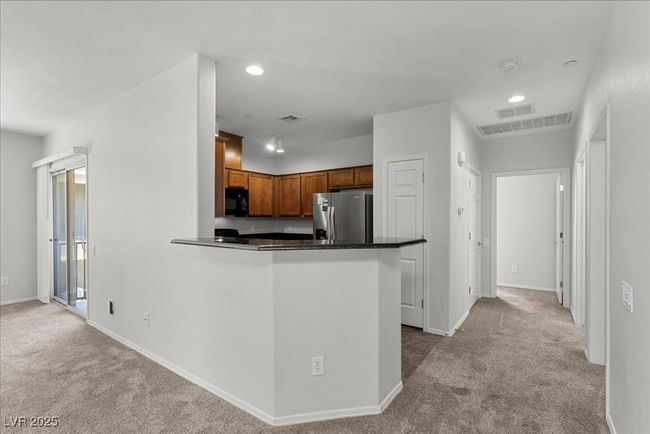 Kitchen with black microwave, stainless steel fridge, light carpet, dark countertops, and brown cabinets | Image 6