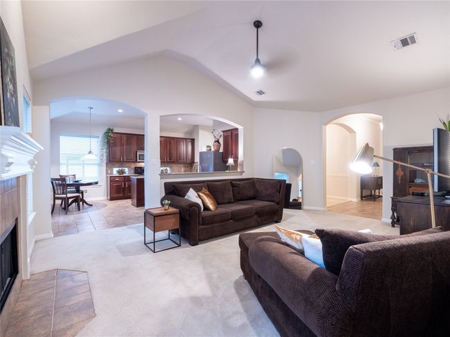 Living area with arched walkways, a wood burning fireplace, light carpet and vaulted ceiling | Image 5