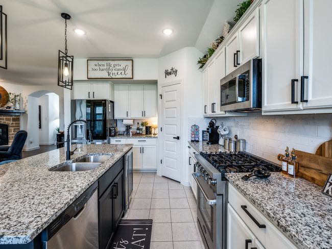 Kitchen featuring backsplash, a sink, arched walkways, appliances with stainless steel finishes, and white cabinetry | Image 17