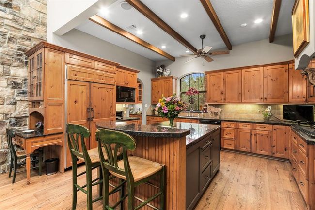 Cast-stone corbels with custom-made wrought iron supports disguise the ventilation system for the Viking gas cooktop. Glass front display cabinets, under-cabinet lighting and exposed ceiling beams add character to this inviting space. A substantial island painted a bold, dark tone provides contrast to the warm wood cabinets and features a breakfast bar on the end from which to entertain the chef. | Image 13