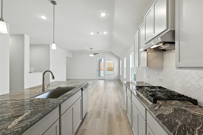 Kitchen featuring stainless steel appliances, under cabinet range hood, light wood-style floors, tasteful backsplash, and vaulted ceiling | Image 7