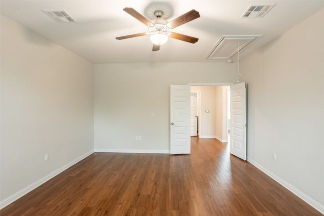Unfurnished room featuring a ceiling fan, visible vents, attic access, and dark wood-type flooring | Image 24