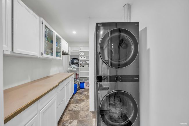 Washroom featuring stacked washing machine and dryer, cabinet space, recessed lighting, and stone finish flooring | Image 21