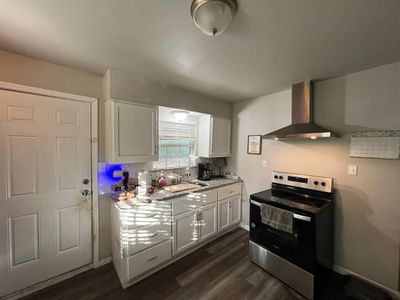 Kitchen featuring wall chimney range hood, sink, electric stove, dark hardwood / wood-style flooring, and white cabinets | Image 3