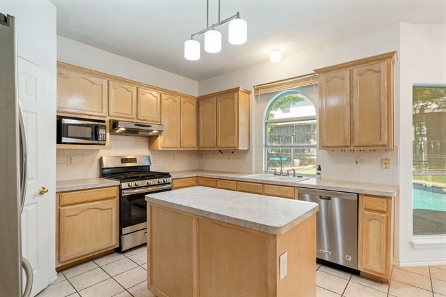 Kitchen with a sink, light countertops, light brown cabinetry, under cabinet range hood, and stainless steel appliances | Image 11