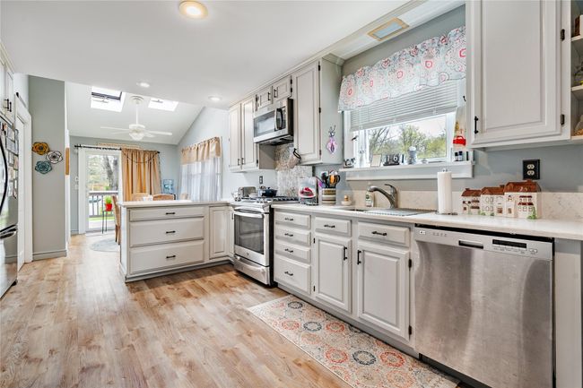 Kitchen with light wood finished floors, light countertops, a sink, a peninsula, and appliances with stainless steel finishes | Image 9