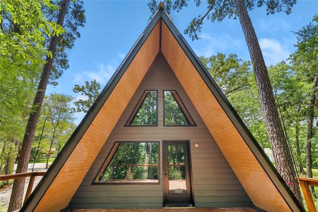 This photo showcases a modern A-frame cabin nestled among tall trees, featuring large triangular windows and a cozy wooden deck, perfect for nature lovers seeking a serene retreat. | Image 5