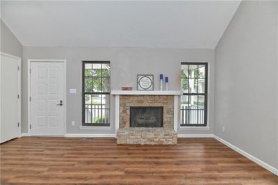 Unfurnished living room featuring a stone fireplace, hardwood / wood-style flooring, and lofted ceiling | Image 3