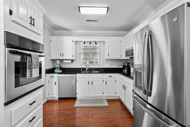 Kitchen with appliances with stainless steel finishes, dark countertops, a sink, white cabinets, and crown molding | Image 10