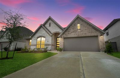 Charming single-story home featuring a striking brick facade, an inviting arched entryway, and a two-car garage, all set against a vibrant sunset sky. | Image 1