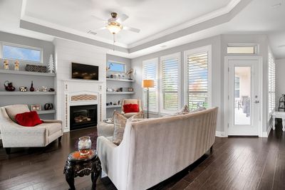 Living room with dark wood-type flooring, a large fireplace, and a raised ceiling | Image 3