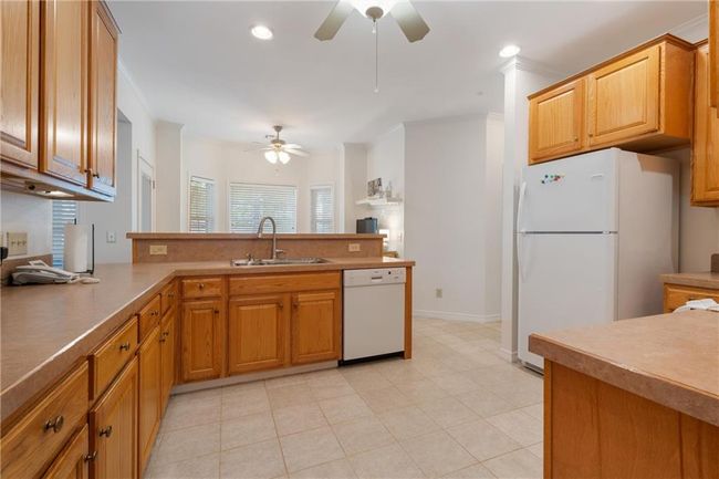 Kitchen with white appliances, a peninsula, a sink, and a ceiling fan | Image 13