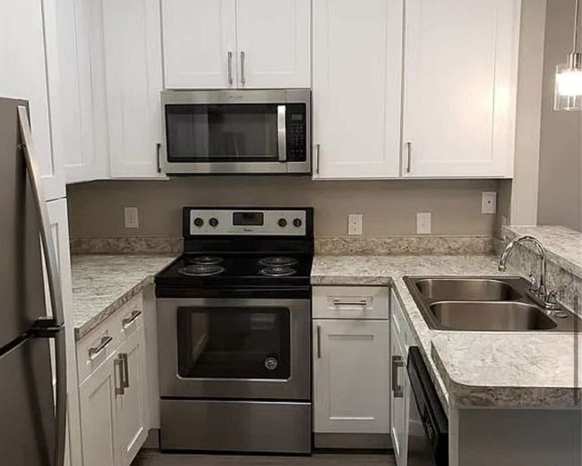 Kitchen with appliances with stainless steel finishes, a sink, light countertops, white cabinets, and hanging light fixtures | Image 4