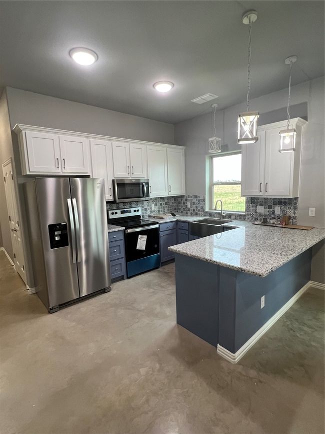 Kitchen featuring white custom cabinets, granite countertops decorative light fixtures, fridge, and stainless steel range oven | Image 33