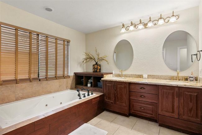 Spacious bathroom with a luxurious soaking tub, double vanity with granite countertops, elegant wood cabinetry, and stylish lighting. | Image 28